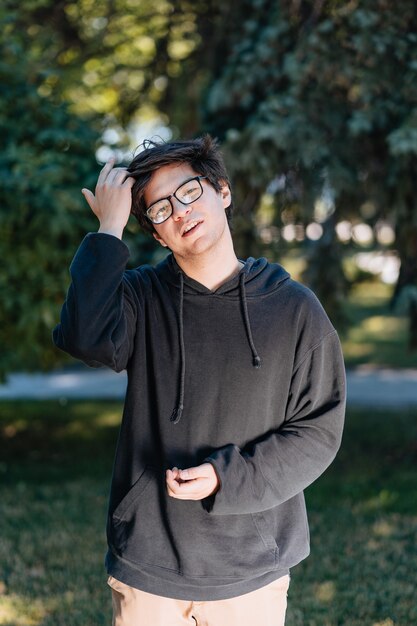 Porträt eines glücklichen jungen männlichen Studenten mit Brille im lässigen Outfit, der im Park posiert.