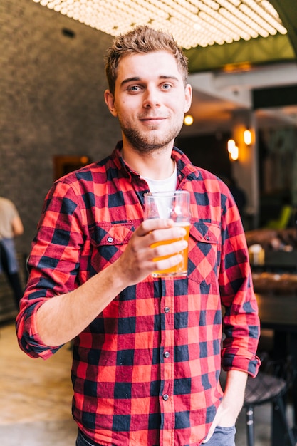 Kostenloses Foto porträt eines glücklichen jungen mannes, der das bierglas betrachtet kamera hält