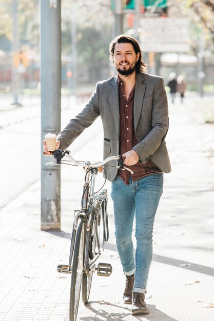 Porträt eines glücklichen jungen Mannes, der mit Fahrrad auf Stadtstraße geht