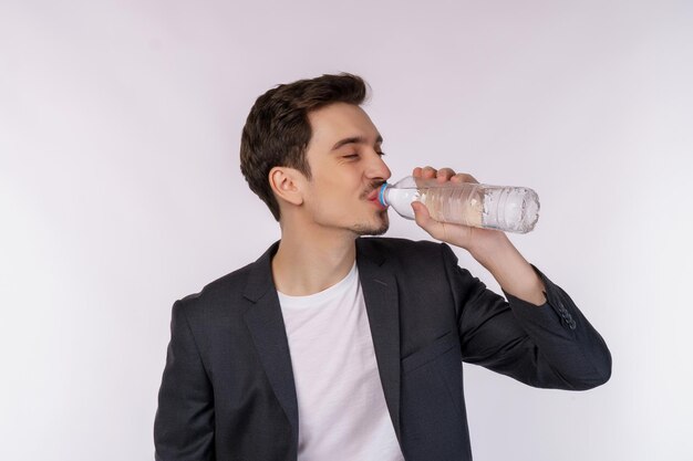 Porträt eines glücklichen jungen Mannes, der Wasser aus einer Flasche trinkt und die Kamera einzeln auf weißem Hintergrund betrachtet