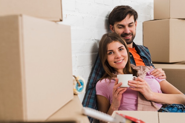 Porträt eines glücklichen jungen Paares, das zwischen den beweglichen Pappschachteln in ihrem neuen Haus sitzt