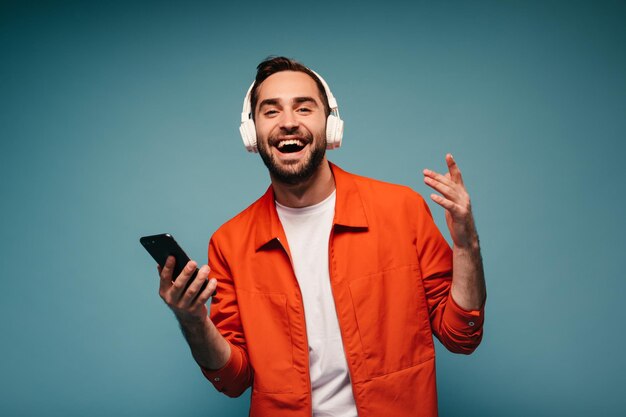 Porträt eines glücklichen Kerls mit Kopfhörern, der ein Smartphone hält