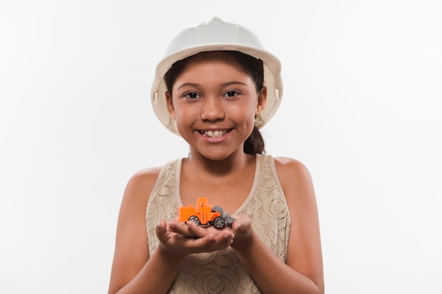 Kostenloses Foto porträt eines glücklichen mädchens im weißen hardhat, der handelsfahrzeugspielzeug hält