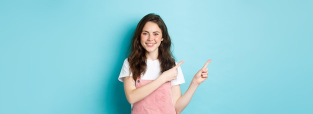 Porträt eines glücklichen Teenager-Mädchens im Sommer-Outfit mit süßem Rouge und hellem Make-up, das mit dem Finger zeigt