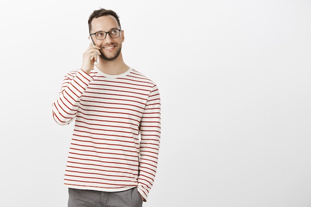 Porträt eines gut aussehenden freundlichen Mannes in der trendigen Brille und im lässigen Outfit, die beim Anrufen eines Freundes über das Smartphone nach oben schauen