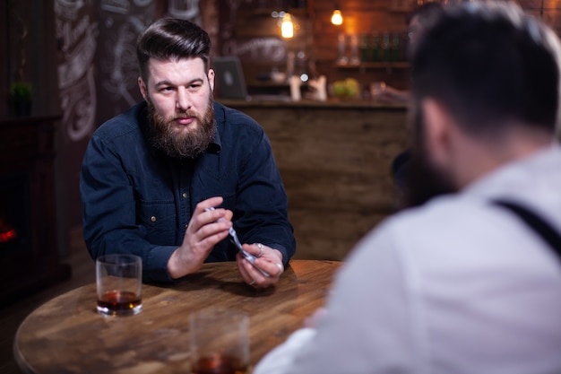 Porträt eines gutaussehenden bärtigen mannes, der in einer kneipe spielkarten mischt. glas whisky, stilvoller mann. eleganter mann.