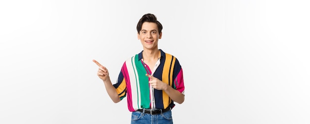Porträt eines gutaussehenden jungen Mannes in stylischer Kleidung, der mit dem Finger nach links zeigt und lächelt und Werbung zeigt