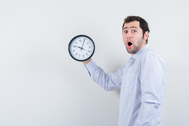 Porträt eines gutaussehenden jungen Mannes in weiß gemustertem Hemd, der Uhr zeigt und sich Sorgen um die Zeit macht, isoliert auf weißem Hintergrund