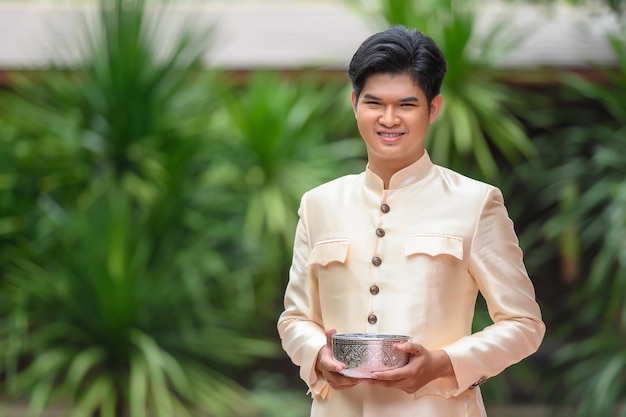 Porträt eines gutaussehenden Mannes in schönen thailändischen Kostümen, der mit einer Wasserschüssel steht, die im Tempel am Songkran-Festival am thailändischen Neujahrs-Familientag im April steht