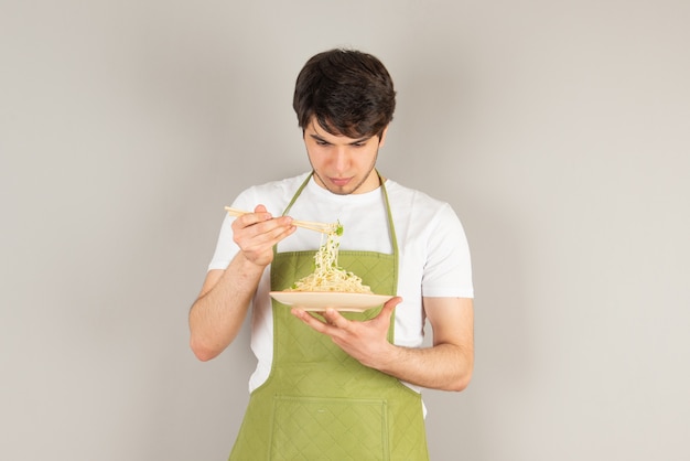 Porträt eines gutaussehenden Mannmodells in der Schürze, die einen Teller mit Essen hält.