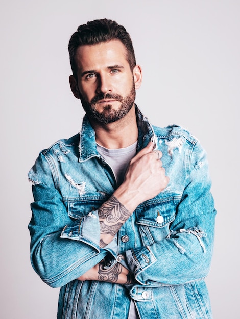 Kostenloses Foto porträt eines gutaussehenden, selbstbewussten, stilvollen hipster-lambersexual-modells sexy mann in jeansjacke gekleidet mode männlich isoliert auf grauem hintergrund im studio