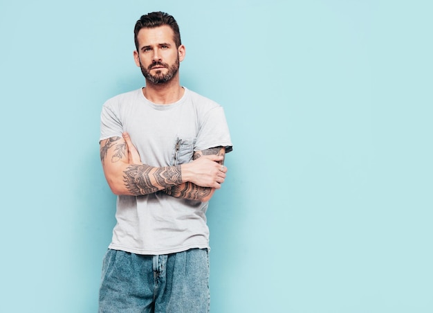 Porträt eines gutaussehenden, selbstbewussten, stilvollen Hipster-Lambersexual-Modells Sexy Mann in T-Shirt und Jeans gekleidet Mode männlich isoliert auf blauer Wand im Studio