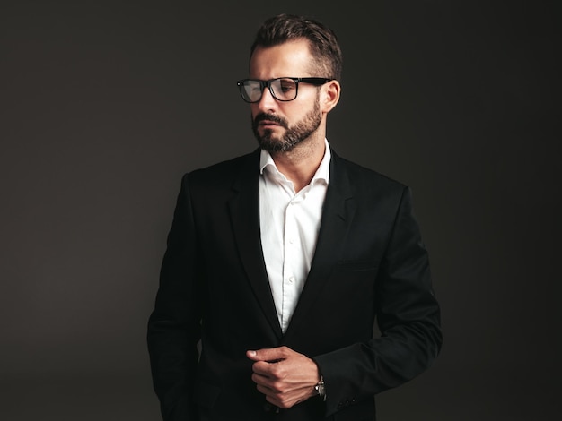 Porträt eines gutaussehenden, selbstbewussten, stilvollen Hipster-Lambersexual-Modells Sexy moderner Mann in elegantem schwarzem Anzug gekleidet Modemann posiert im Studio auf dunklem Hintergrund In Brillen