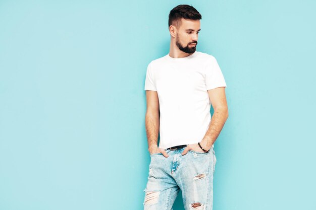 Porträt eines gutaussehenden, selbstbewussten, stilvollen Hipster-Lambersexual-ModelsMann in weißem T-Shirt und Jeans Modemann isoliert auf blauer Wand im Studio