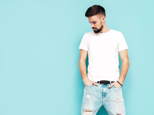 Porträt eines gutaussehenden, selbstbewussten, stilvollen Hipster-Lambersexual-ModelsMann in weißem T-Shirt und Jeans Modemann isoliert auf blauer Wand im Studio