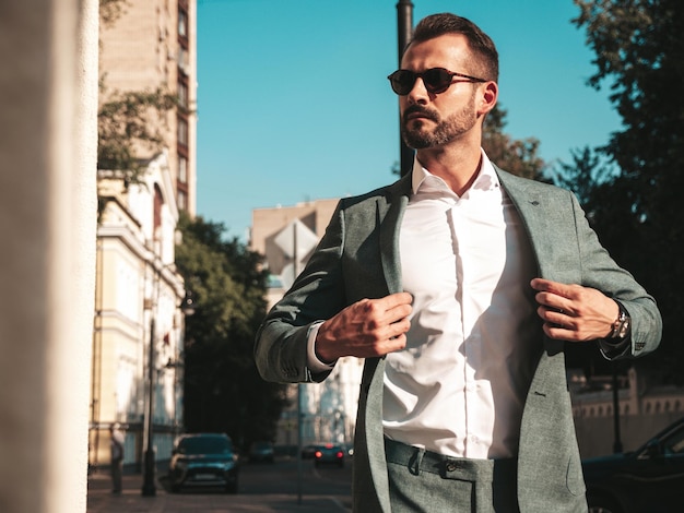 Porträt eines gutaussehenden, selbstbewussten, stilvollen Hipster-Lambersexuellen ModelsSexy moderner Mann in elegantem Anzug gekleidet Modemann posiert im Straßenhintergrund in Europa-Stadt bei Sonnenuntergang mit Sonnenbrille