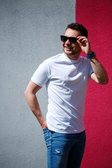 Porträt eines gutaussehenden, stilvollen mannes, ein mann in einem weißen, leeren t-shirt, der auf einem grauen und roten wandhintergrund steht. urbaner kleidungsstil, modernes modisches bild. männermode