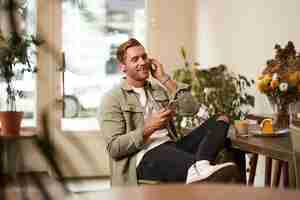 Kostenloses Foto porträt eines hübschen, glücklichen jungen mannes, der sich in einem café entspannt und zeit im café verbringt, um zu hören