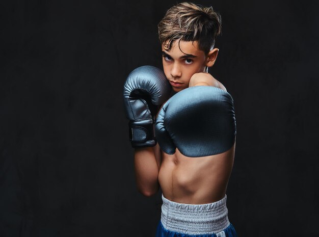 Porträt eines hübschen, hemdlosen jungen Boxers mit Handschuhen. Getrennt auf dem dunklen Hintergrund.