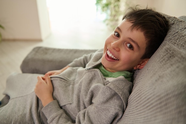 Porträt eines hübschen kaukasischen teenagers, der mit einem fröhlichen lächeln lächelt, während er sich zu hause auf einem sofa im wohnzimmer entspannt