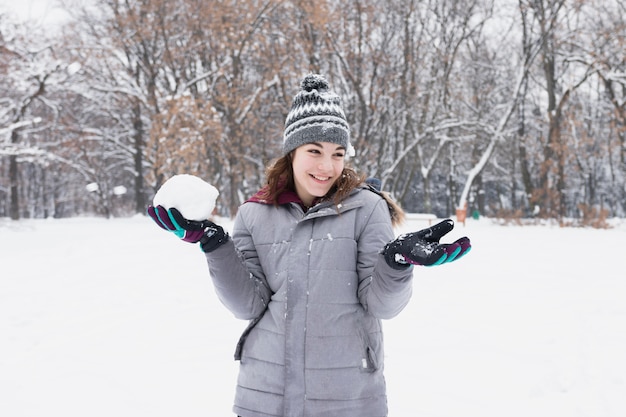 Kostenloses Foto porträt eines hübschen lächelnden mädchens, das schneeball am wald hält