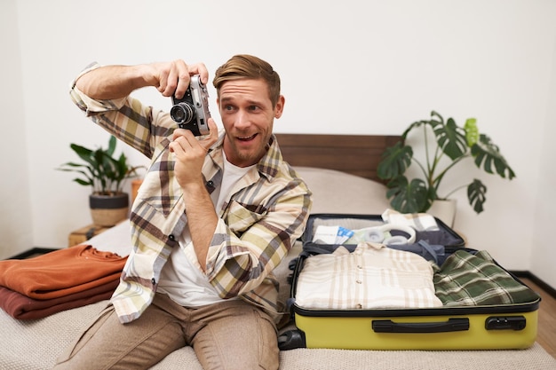 Kostenloses Foto porträt eines hübschen mannes, der auf urlaub fährt, einen koffer packt und eine kamera in der hand hält.