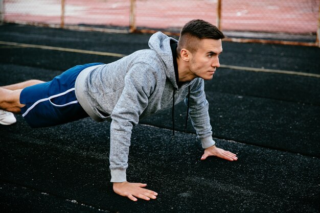 Porträt eines hübschen Sportlers des Sitzes, der Plankenübung tut, übend, drückt auf Spurstraße hoch