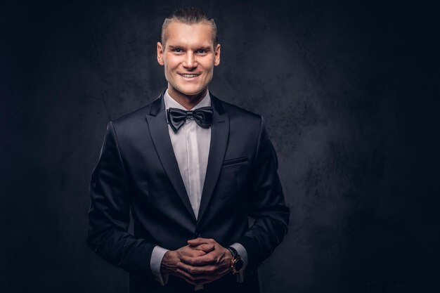 Porträt eines hübschen, stilvoll lächelnden Mannes in einem eleganten schwarzen Anzug vor dunklem Hintergrund.