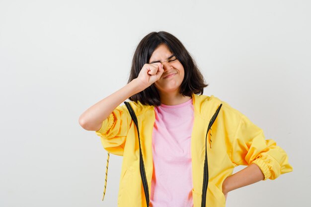 Porträt eines jugendlichen Mädchens, das ihr Auge in T-Shirt, Jacke reibt und müde Vorderansicht schaut