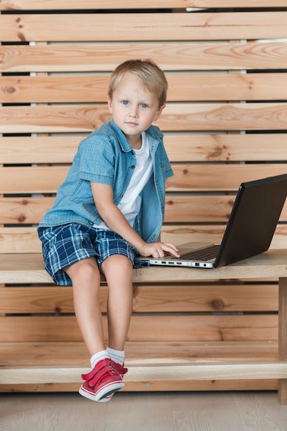 Porträt eines Jungen, der auf Bank unter Verwendung des Laptops sitzt