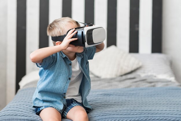 Porträt eines Jungen, der auf tragenden Schutzbrillen der virtuellen Realität des Betts sitzt