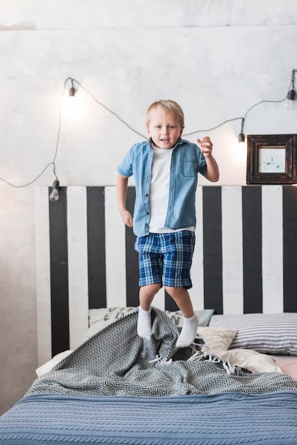 Porträt eines Jungen, der über Bett mit verziertem belichtetem Licht auf Wand springt