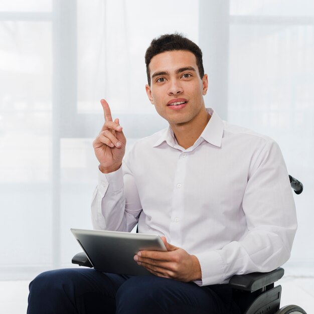 Porträt eines jungen Geschäftsmannes, der auf dem Rollstuhl hält digitale Tablette in der Hand hält seinen Finger aufwärts sitzt