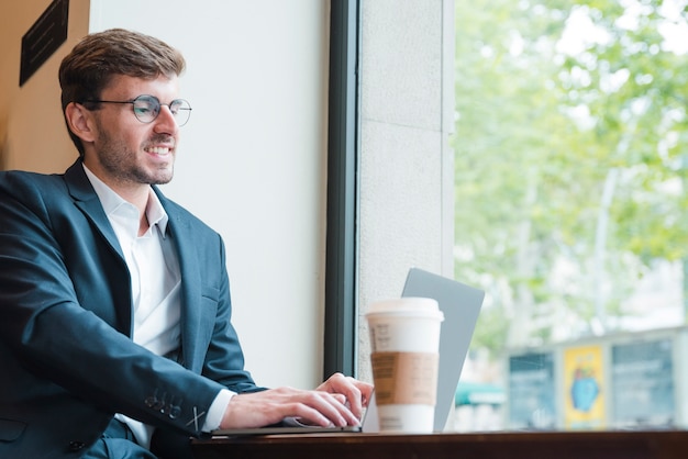 Porträt eines jungen geschäftsmannes unter verwendung des laptops mit kaffeetasse auf tabelle im café