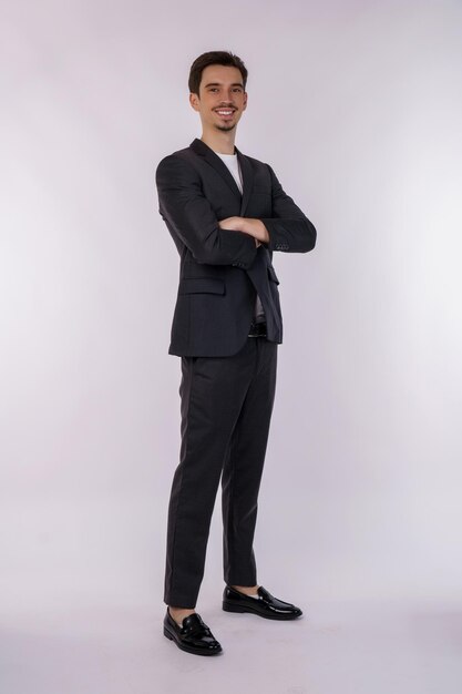 Porträt eines jungen, gutaussehenden Geschäftsmannes im Anzug, der mit verschränkten Armen steht, isoliert auf weißem Studiohintergrund