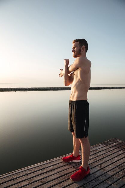 Porträt eines jungen hemdlosen Sportlers, der sich vor dem Joggen aufwärmt