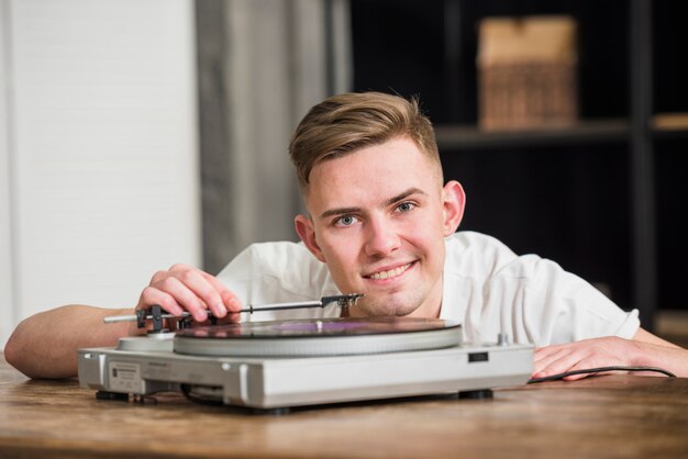 Porträt eines jungen hübschen lächelnden Mannes, der den Schallplattenspieler der Drehscheibe spielt