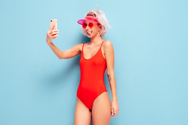 Porträt eines jungen, lächelnden, blonden Modells im roten Badeanzug der Sommerbadebekleidung und einer transparenten Schirmmütze. Sexy sorglose Frau, die Spaß hat und verrückt wird