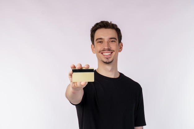 Porträt eines jungen, lächelnden, gutaussehenden Mannes in Freizeitkleidung, der die Kreditkarte isoliert auf weißem Hintergrund zeigt
