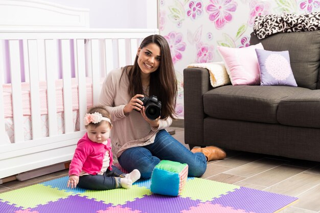 Porträt eines jungen lateinamerikanischen Babyfotografen, der Fotos von einem kleinen Mädchen in einem Kinderzimmer macht