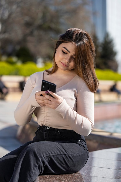 Porträt eines jungen Mädchens, das ein Telefon hält und im Park sitzt Foto in hoher Qualität