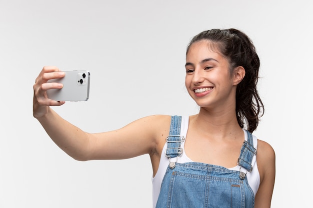 Kostenloses Foto porträt eines jungen mädchens in overalls, das ein selfie mit dem smartphone macht