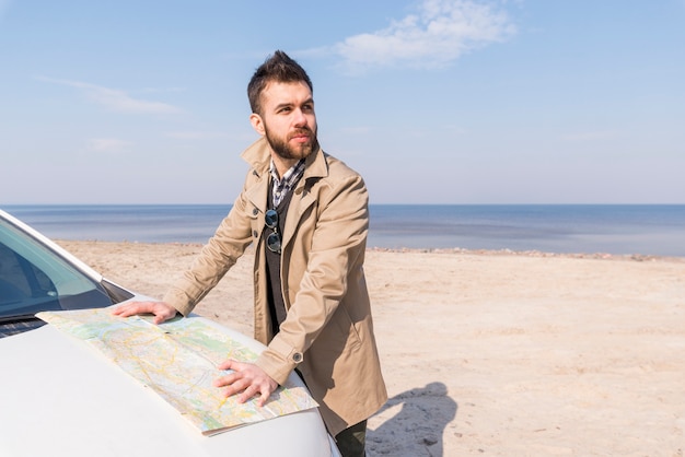 Porträt eines jungen männlichen Reisenden, der auf dem Strand mit Karte steht