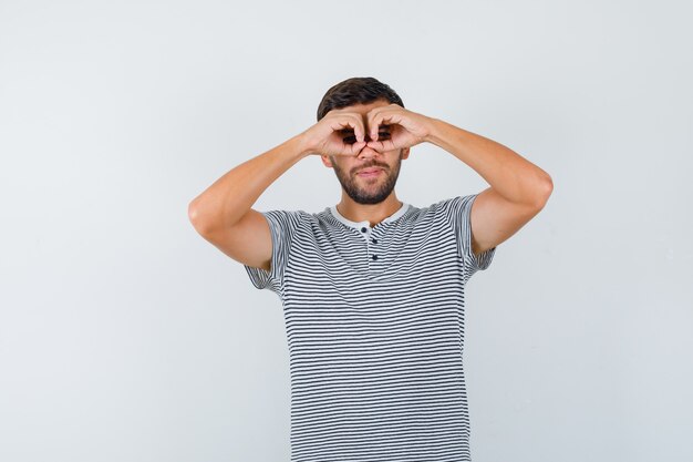 Porträt eines jungen Mannes, der eine Brillengeste im T-Shirt zeigt und sich wunderte Vorderansicht