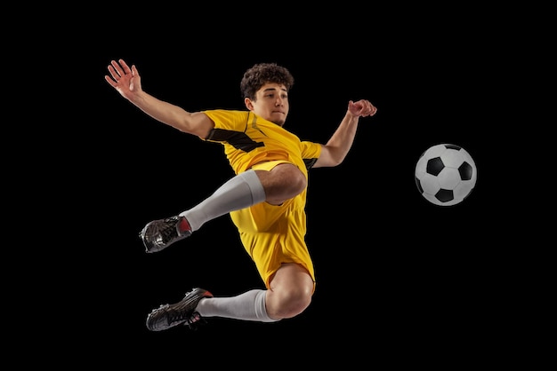 Porträt eines jungen Mannes, der im Bewegungstraining Fußball spielt, isoliert über schwarzem Studiohintergrund Kicking Ball