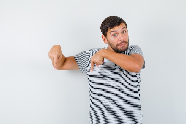 Porträt eines jungen Mannes, der in gestreiftem T-Shirt nach unten zeigt und ahnungslose Vorderansicht schaut