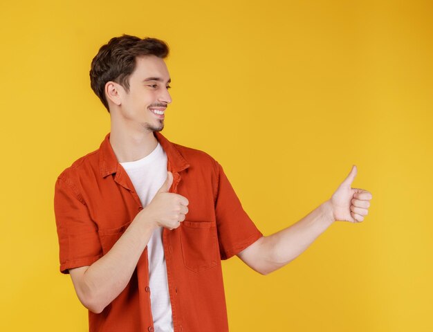 Porträt eines jungen Mannes, der mit dem Finger auf den Kopierraum zeigt, der auf gelbem Studiohintergrund isoliert ist