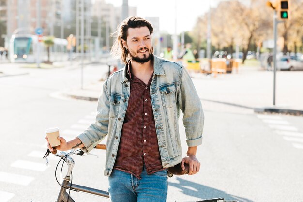 Porträt eines jungen Mannes, der nahe dem Fahrrad auf der Straße steht