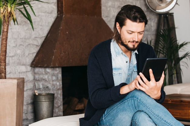 Porträt eines jungen Mannes, der zu Hause sitzt, seinen Handy grastend