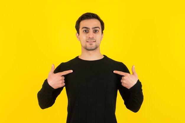 Porträt eines jungen Mannes im schwarzen Sweatshirt, der an der gelben Wand steht und vor der Kamera posiert